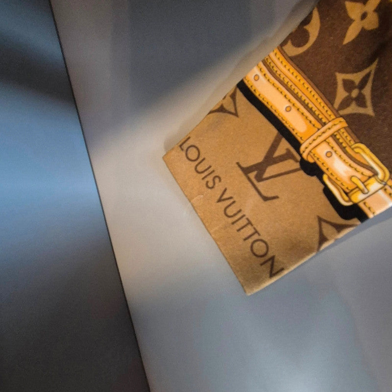 Extrémité du bandeau Confidentiel – détail boucle jaune et logo Louis Vuitton sur fond beige