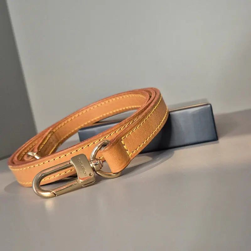 Bandoulière Louis Vuitton en cuir naturel – vue générale enroulée sur fond neutre