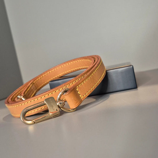 Bandoulière Louis Vuitton en cuir naturel – vue générale enroulée sur fond neutre