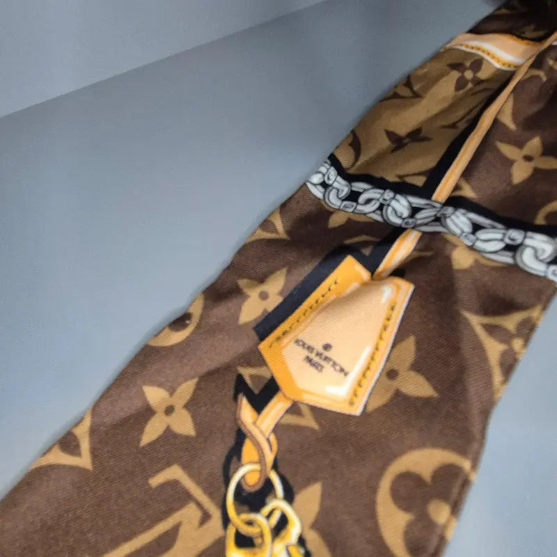 Motif imprimé Louis Vuitton avec étiquette graphique et chaîne dorée sur fond Monogram